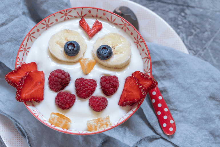 A bowl of yogurt with fruit on top, including banana, blueberries, strawberries and oranges.