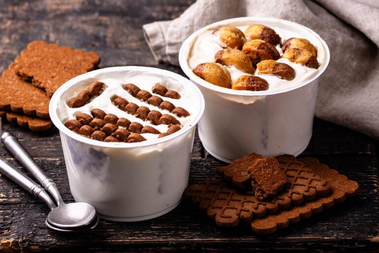 Two yogurt pots of the viral 2-ingredient Japanese Cheesecake recipe sitting on a wooden table beside two teaspoons and some cookie