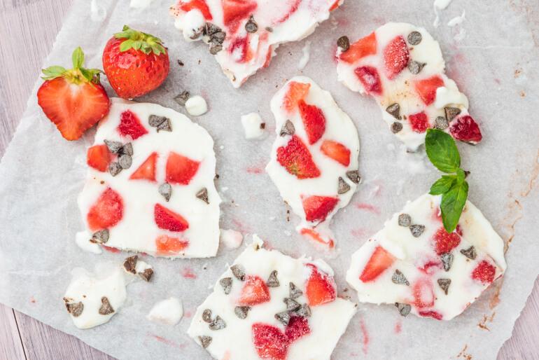 Broken pieces of frozen yogurt bark sitting on a chopping board on a table with strawberries