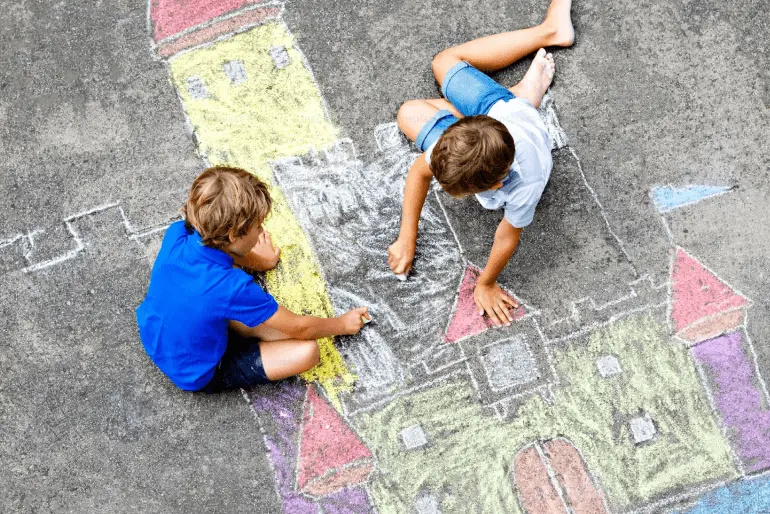 Two small children drawing a castle with chalk on the sidewalk.